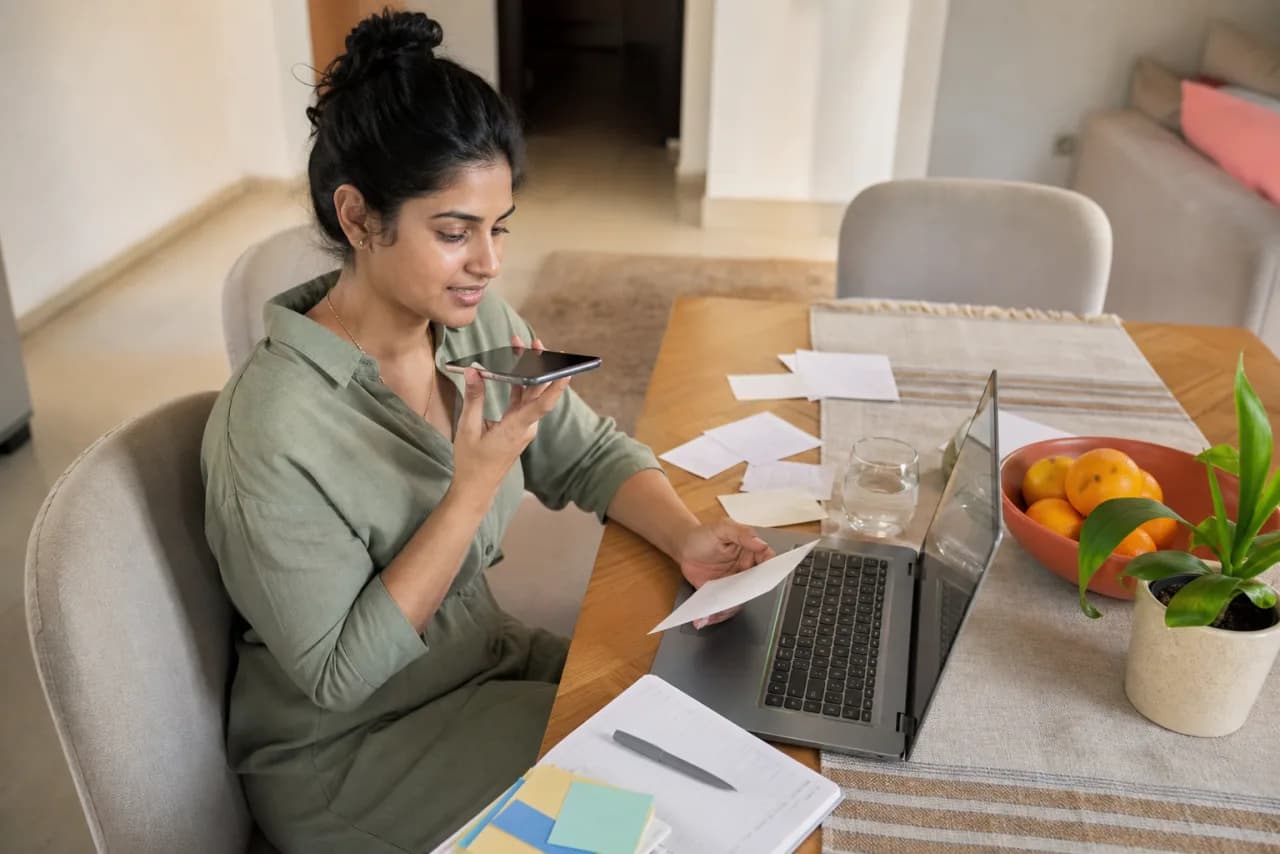 A Telugu-speaking adult dictating household planning notes while sorting paper reminders
